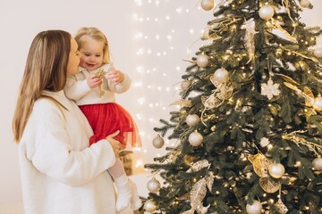 Mother holding daughter decorating christmas tree with golden ornaments