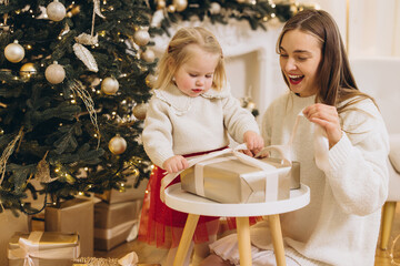 Mother and daughter opening christmas gift near decorated tree