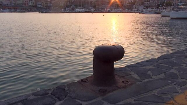 A bollard of the pier with the village in the background. Marina di Camerota harbor at sunset. Salerno, Italy.