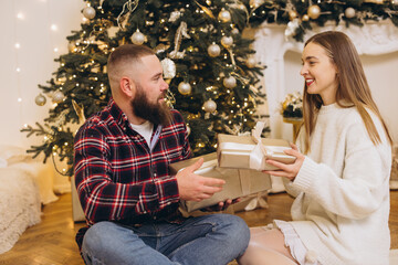 Couple exchanging christmas gifts near decorated tree