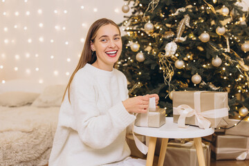 Smiling woman wrapping christmas gifts near decorated tree