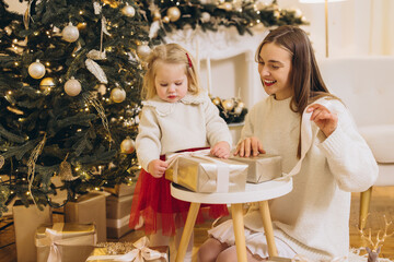 Mother and daughter wrapping christmas gifts by the tree