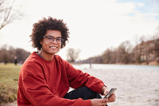 Gen Z boy outside hanging around beside a river and smiling at the camera. Munich, Germany