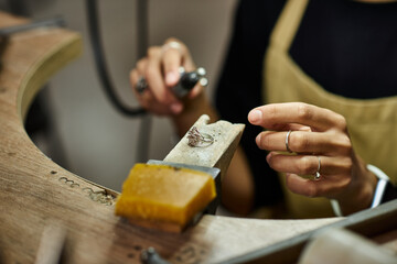 A talented woman intricately shapes a beautiful piece of jewelry in her warm, inviting workspace.