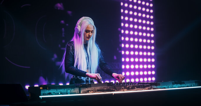 Portrait of a Beautiful DJ Making a Show on a Vibrant Stage, Entertaining a Large Audience in a Concert Hall. Music Producer Dancing on Stage and Using Turntables to Mix the Party Songs
