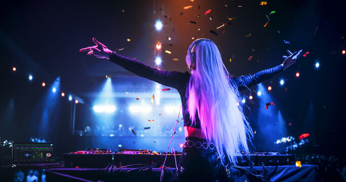 Young Beautiful Female DJ Playing Dance Music Sets, EDM, Techno, House Tracks at a Nightclub with Devoted Music Fans. Neon Lights, Confetti and Excited Crowd Create a Party Atmosphere at a Festival