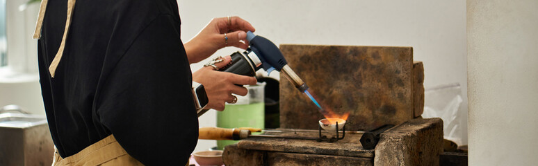 A woman using torch in a warm studio filled with creating tools.