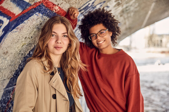 Gen Z couple outside under a bridge smiling at the camera. Munich, Germany
