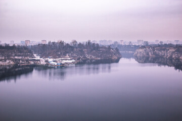 Obraz premium Fantastic purple landscape of the lake and the little workers buildings in the quarry, homes of the big city in the background