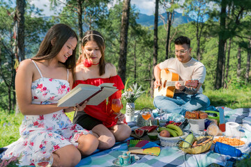 Happy and young friends enjoying picnic in the nature woods with food drinks guitar and books around
