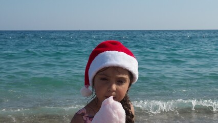 Happy boy in a santa claus hat plays beach. A child in Christmas is resting on the sea. Christmas vacation on tropical island. Xmas vacation. Winter holidays. Travel with children. Merry Christmas