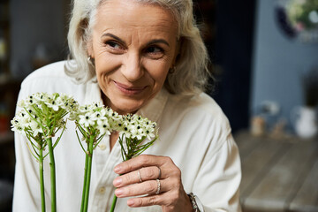 A joyful mature woman enjoys the fragrance of beautiful flowers in her hands, radiating happiness.