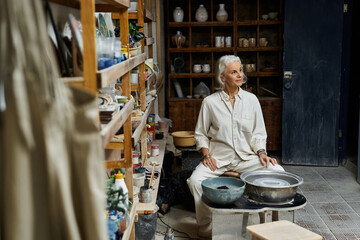 An elegant mature woman focuses on her pottery craft amidst a well organized studio space.