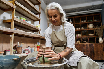 The mature woman shapes clay into a beautiful pot while enjoying her creative process.
