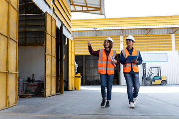 Two construction workers wearing orange vests walk down a yellow hallway