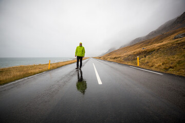 Ein Mann schlendert auf einer einsamen Straße zwischen Meer und Hügeln im Regen