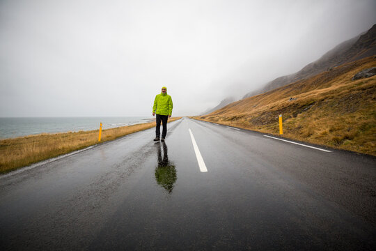 Ein Mann schlendert auf einer einsamen Stra&szlig;e zwischen Meer und H&uuml;geln im Regen