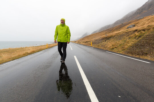 Ein Mann mit Regenjacke auf einer einsamen Stra&szlig;e in einer einsamen Gegend