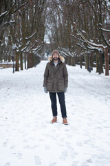 Hombre joven con ropa de invierno (Abrigo, gorro y botas) en jardin nevado con árboles de fondo en Zaragoza (España)