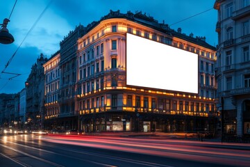 Large blank billboard on a building facade illuminated by city lights during the evening in an urban setting with a blurred background