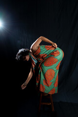Portrait of beautiful woman standing on wooden stool wearing colorful outfit making body movements.