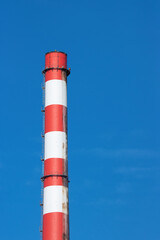 red and white industrial chimney stack against a blue sky