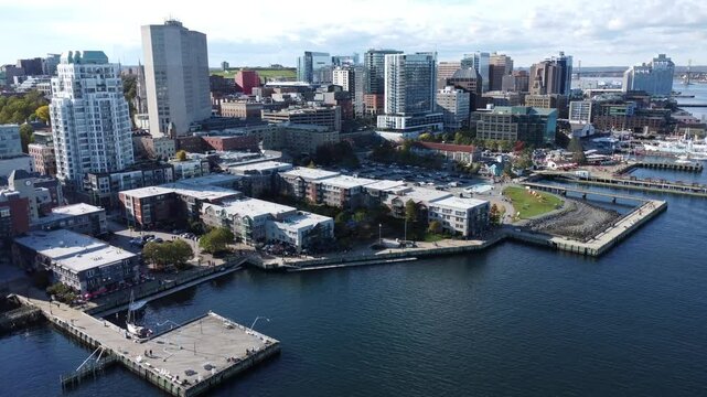 Cinematic drone aerial footage descending showing waterfront docks and buildings, the port and sighseeing ships in Halifax, Nova Scotia, Canada during summer season.