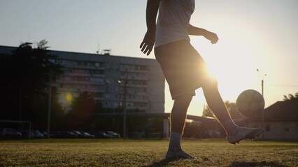 Legs of young man kicking ball at green field. Male feet of professional footballer juggling soccer...