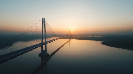 Obraz premium A modern suspension bridge spanning a vast river at sunset.