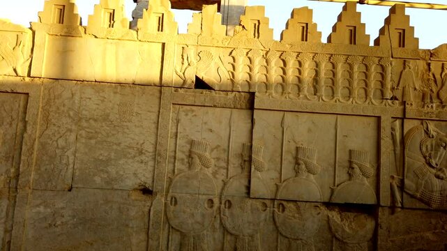 Sunlight slowly illuminates the intricate carvings of soldiers and animals on a wall at persepolis