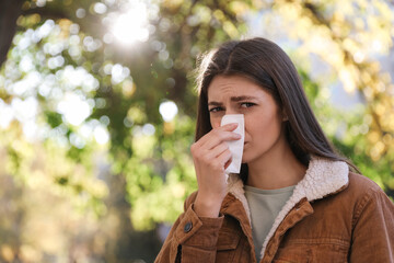 Woman with runny nose in park, space for text