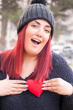 Portrait of a sedactive redhead with woolen hat in the park, holding a red heart
