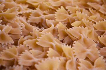 raw pasta in the shape of bows on a black background. The paste has a textured surface and a delicate light yellow tint. Pasta background and texture.