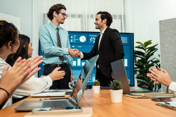 Two businessman shake hand in meeting room with coworker give cheerful applause. Team of analyst...