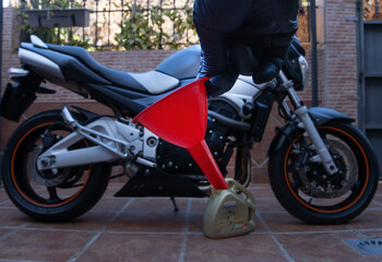 A hand with black latex gloves, holding a funnel to change the engine oil of a motorcycle. A motorcycle in the background. Maintenance concept.