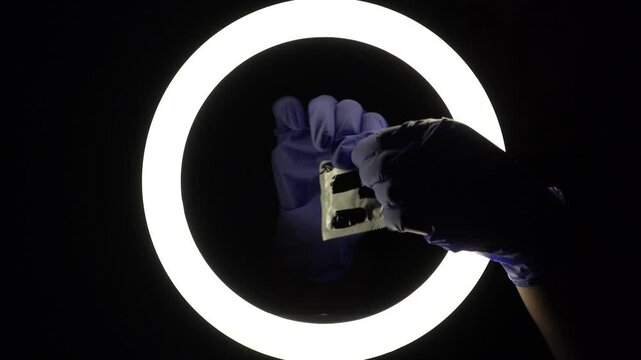 female hands in blue rubber latex gloves open, unfold, stretch and test the strength of a condom close-up on a black background. protection against sexually transmitted diseases and contraception