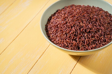 Close-up of a bowl of red rice is placed on a yellow table.The raw rice is spread out in the bowl, copy-space.