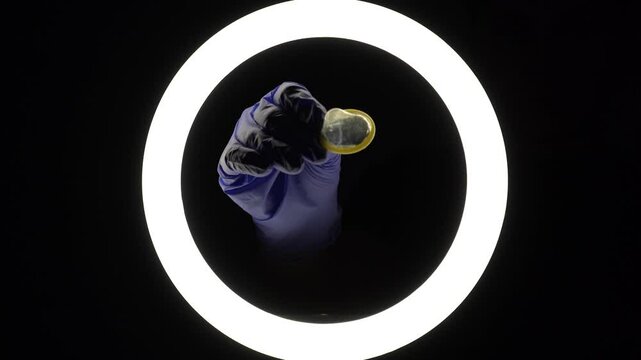 female hands in blue rubber latex gloves open, unfold, stretch and test the strength of a condom close-up on a black background. protection against sexually transmitted diseases and contraception