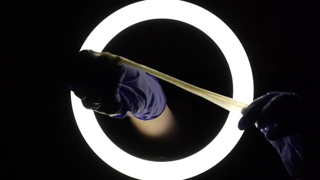 female hands in blue rubber latex gloves open, unfold, stretch and test the strength of a condom close-up on a black background. protection against sexually transmitted diseases and contraception