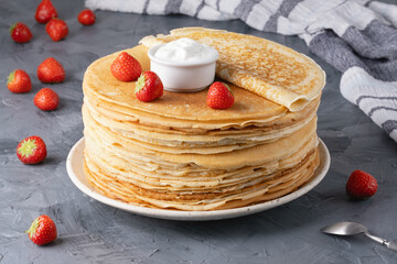 Pancakes with sour cream and strawberries on a grey table