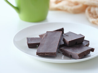A plate of homemade dark chocolate on a table near a mug of coffee.