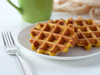 A plate of homemade gluten free waffles on a table near a mug and a fork. Close up.