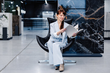 Woman in a light blue suit sitting in a black chair holding a white book in a modern showroom