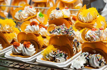 Thai Crispy Pancake. A table with a variety of desserts, including ice cream sandwiches and other treats. The desserts are arranged on a metal rack, and there are several bowls and spoons nearby