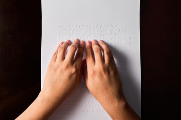 Hands of a blind person reading some braille text touching the relief.