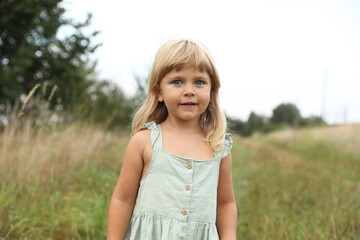 Naklejka premium Portrait of cute little girl at meadow. Child enjoying beautiful nature