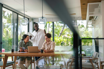 A group of young adult professionals, each from different ethnic backgrounds, collaborate using a...