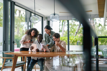 A group of young adult professionals of diverse ethnicities work diligently in a sleek modern office, exchanging ideas over digital devices, reflecting teamwork and strategy.