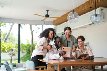 A joyous group of young adult professionals, comprising different ethnicities, is gathered around a table, sharing ideas in a sleek modern office.