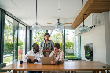 A group of young adults with diverse backgrounds engages in a collaborative project, using laptops and digital tablets, dressed in casual business attire in a well-lit, stylish office space.